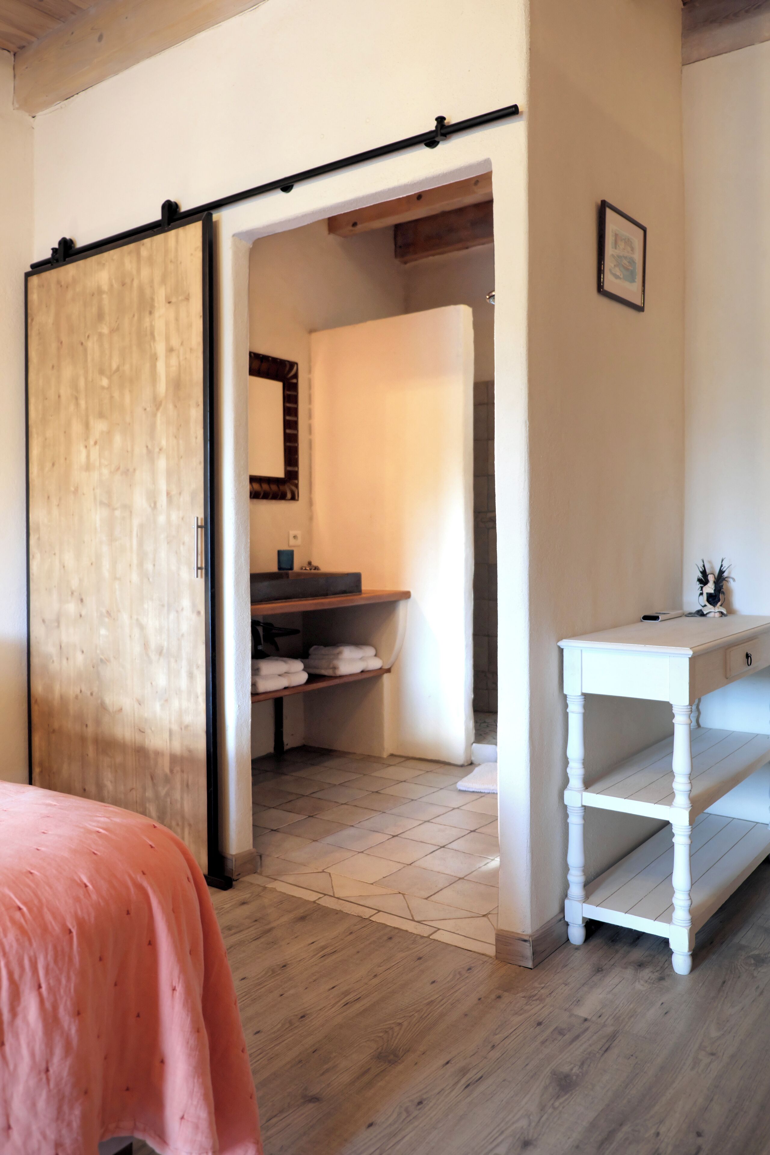 Ein Schlafzimmer mit einer Schiebetür, einem Bett mit rosa Bettwäsche, einer weißen Kommode und einem durchgegangenen Tür einsehbaren Badezimmer.