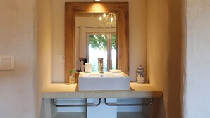 A narrow bathroom with a wooden-framed mirror, a white sink, and a small trash bin.