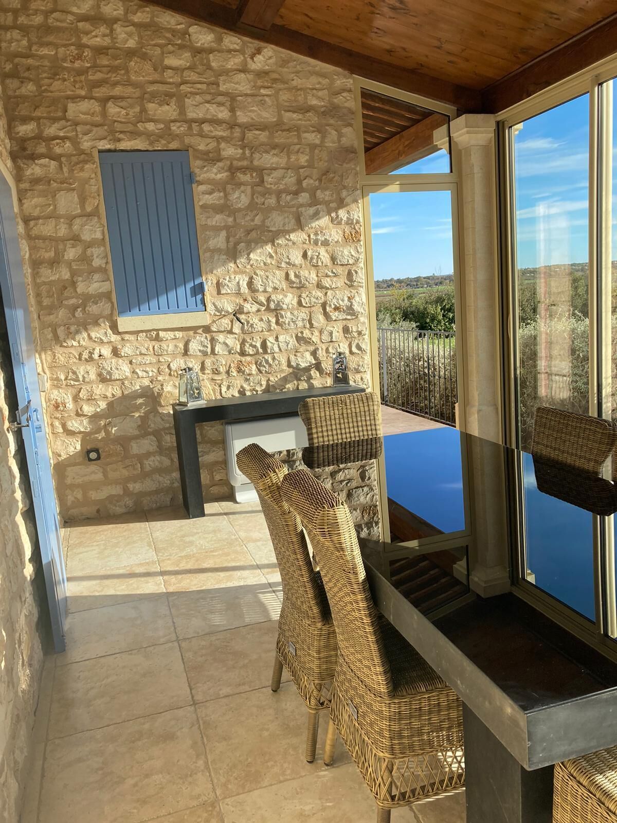 Habitación de paredes de piedra con una mesa y sillas de mimbre, un persiano azul y vistas al paisaje.