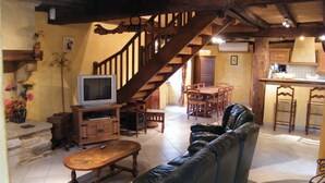 A cozy living room with a leather sofa, wooden coffee table, and a TV on a wooden stand. A wooden staircase leads to a dining area with a table and chairs. - Maison De La Residence Celeste (Ogenne-Camptort)