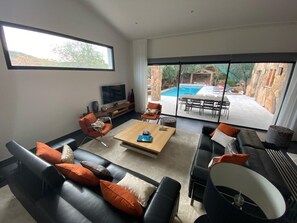 A modern living room with a pool view, featuring a sofa set, a coffee table, and a TV.