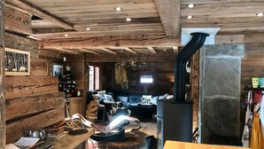 Interior acolhedor de uma cabana com decoração em madeira, lareira de pedra, um sofá e uma mesa de jantar.