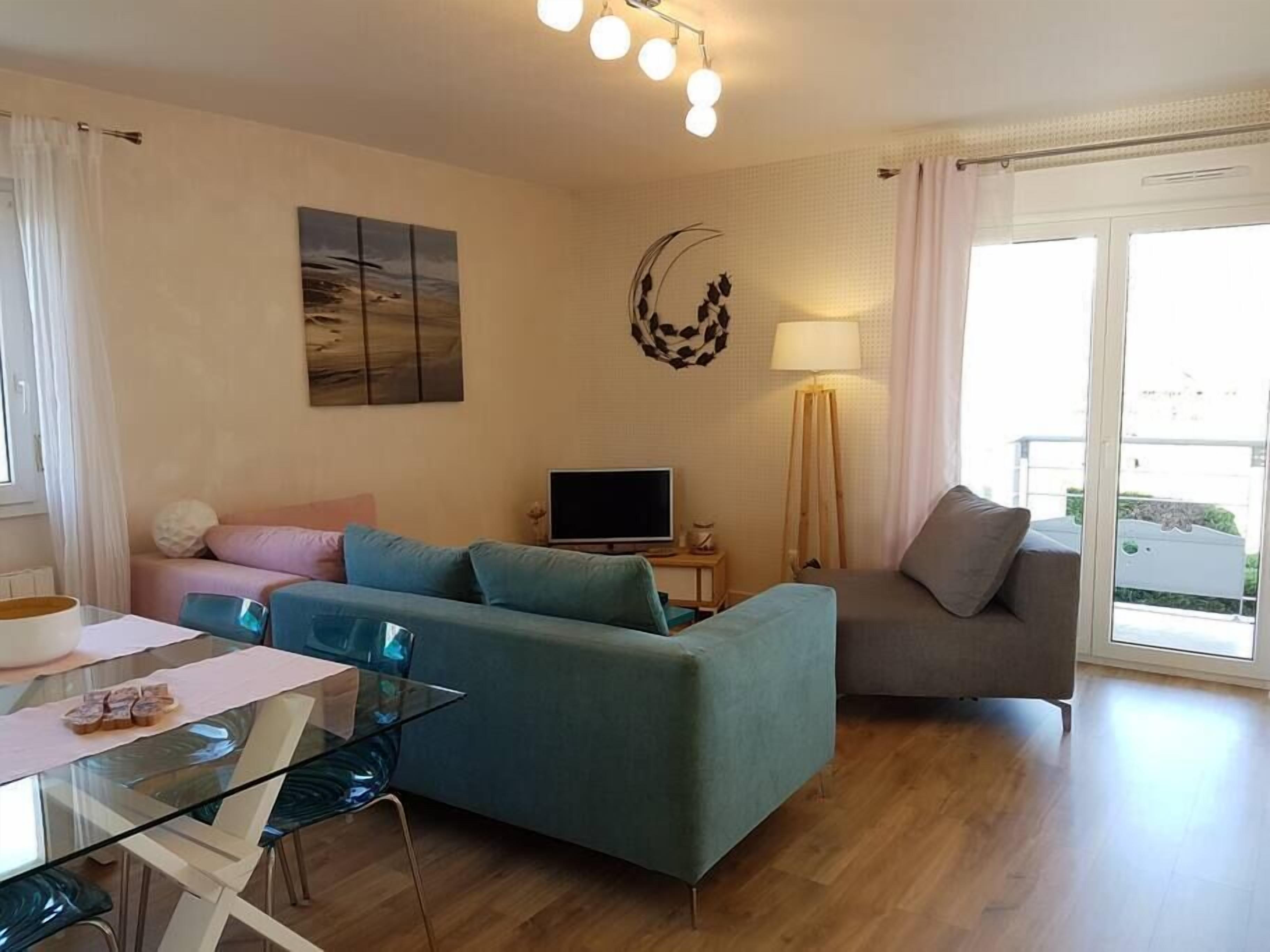 A modern living room with a sofa, a TV, a glass dining table, and a lamp.