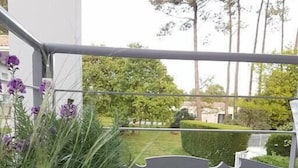 A modern outdoor area with a metal structure, green plants, and a view of a garden and trees.