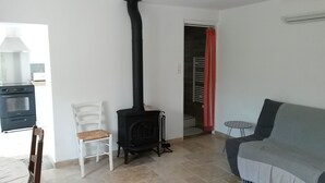 Ein Wohnzimmer mit einem schwarzen Kaminofen, einem weißen Sessel, einem grauen Sofa und einem kleinen runden Tisch.