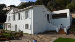 Ein zweistöckiges weißes Haus mit einer Steinterrasse, einer Holztreppe und einer Garage.
