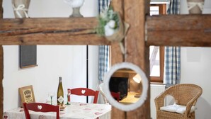 A dining area with a table set for two, a bottle of wine, and a wicker chair. - Rempart - Large studio in the centre of the village (Eguisheim)