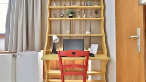 A wooden desk with a computer, a red chair, and a shelf with decorative items. - Rempart - Large studio in the centre of the village (Eguisheim)
