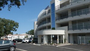 Un edificio a più piani con facciata curva, un ingresso centrale e un parcheggio con diverse auto.