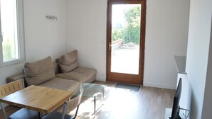 A small, bright room with a wooden table, a sofa, and a television. - The Orange Terrace (Antibes)