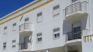 Un edificio de varios pisos con paredes blancas y detalles en amarillo. Varias balcones con barandillas de metal.