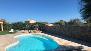 Une piscine avec un mur en pierre et une chaise blanche.
