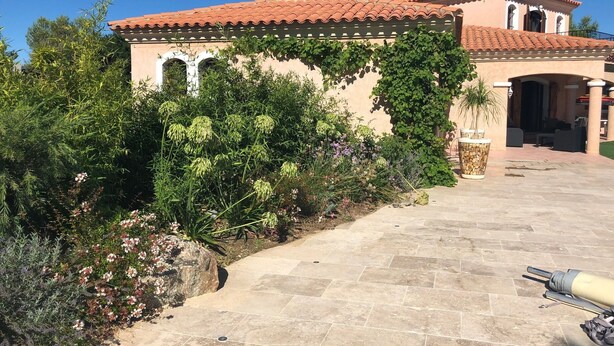 Un bâtiment doté d’un toit recouvert de tuiles rouges, d’une pergola ornée de plantes grimpantes et d’un espace d’entrée pavé.