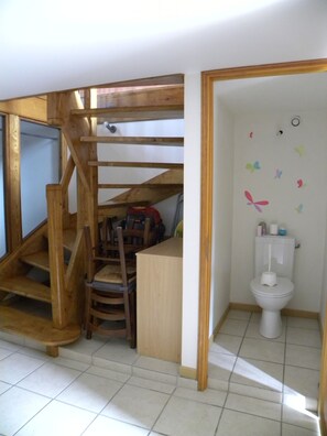 A wooden staircase leading to a lofted area with a toilet and a chair.