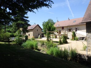 A stone building with a sloped roof, surrounded by greenery and a fenced area.