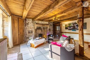 A rustic interior with stone walls, wooden beams, a fireplace, a dining table, and a sofa.