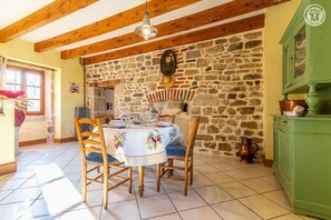 A dining area with a stone wall, wooden ceiling beams, and a table set for two. - "6 PEOPLE, LES PERRIERES, BURGUNDY SAS MAYMARD ANTULLY 0611375830 (3 vacation rentals = 17 people)" (Antully)