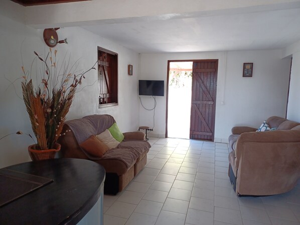 A living room with a sofa, a coffee table, and a TV. There's a wooden door and a window with a view. - Villa between two seas for rent (Saint François)