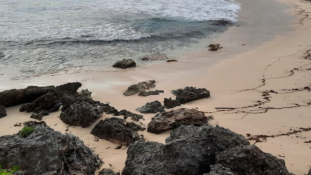 Une plage avec des affleurements rocheux et une croix sur une colline en arrière-plan.