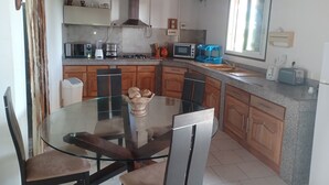 Une cuisine moderne dotée de plans de travail en granit, d’armoires en bois, d’une table à manger en verre et d’une cuisinière encastrée.