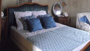 Un dormitorio con estructura de cama de madera, colcha estampada y pared de piedra.
