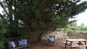 Un banco de madera con cojines estampados, un muro de piedra y una mesa de picnic en un jardín.