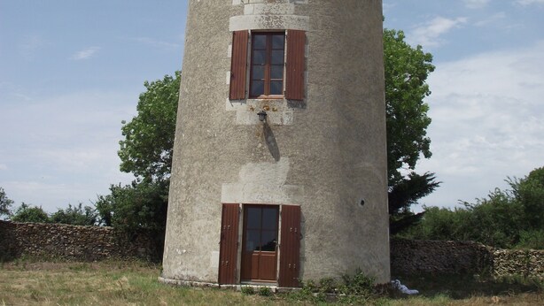 Una torre alta y cilíndrica con techo cónico, con varias ventanas y contraventanas de madera, sobre un cielo despejado.