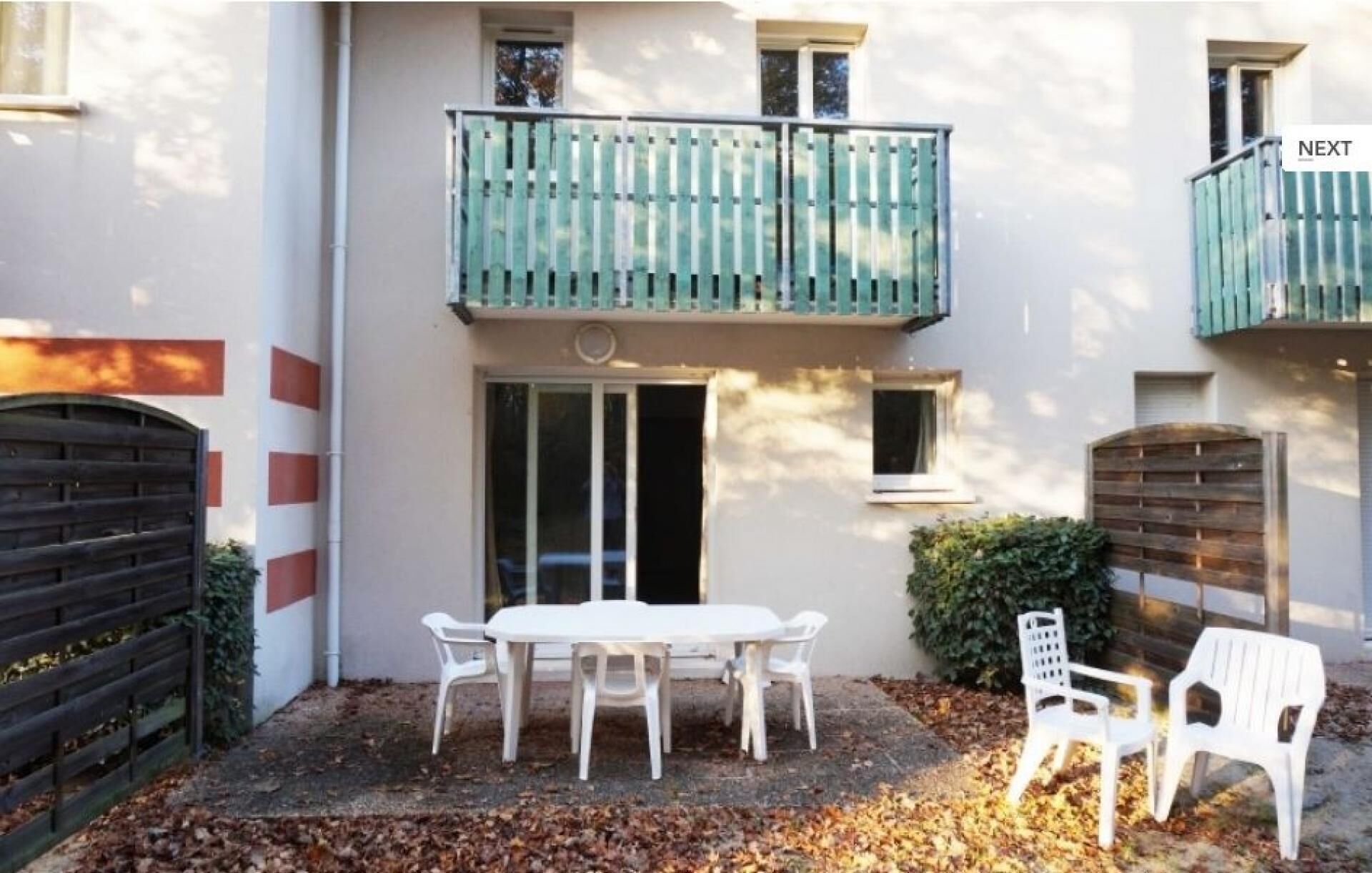 A two-story building with a balcony, a table with chairs, and a gate.