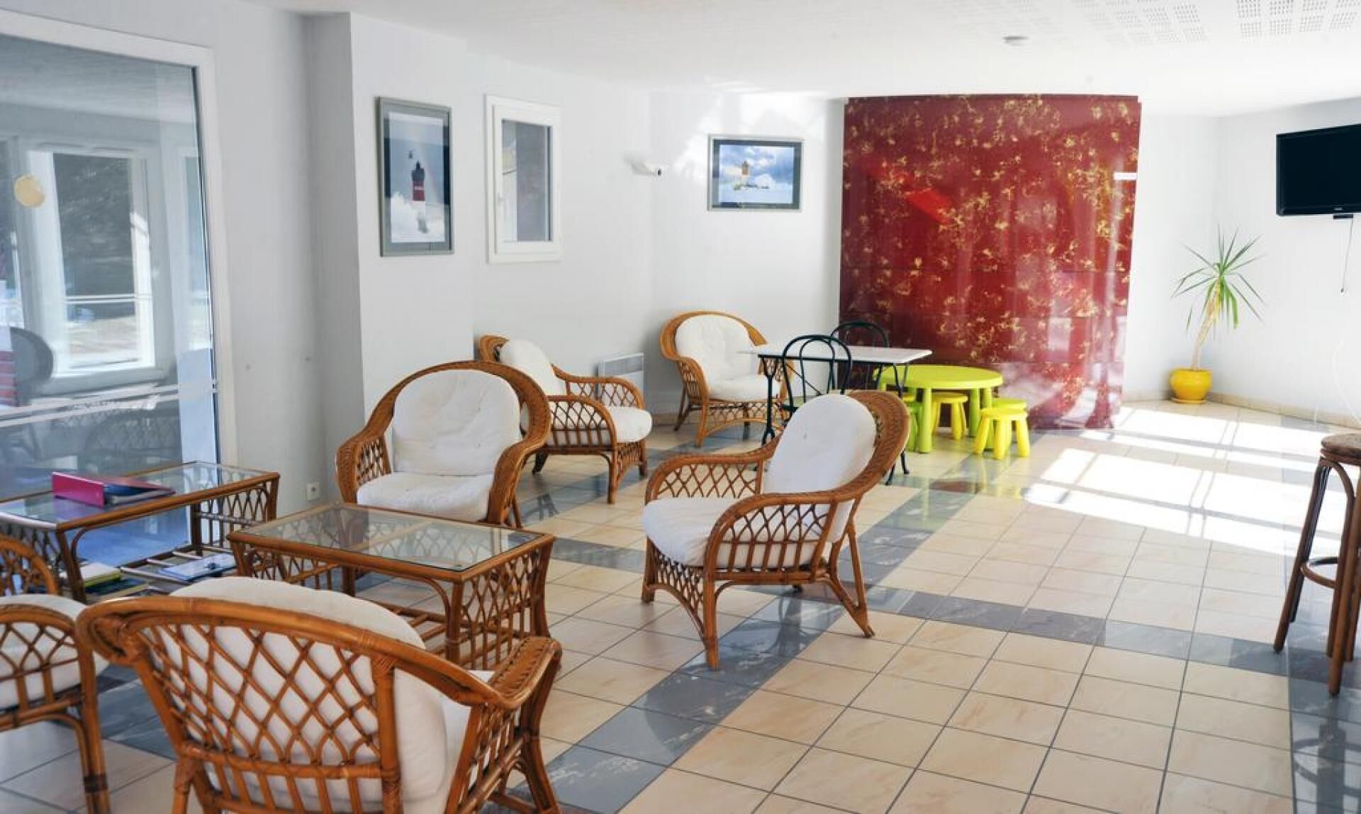 A room with wicker chairs, a glass table, a yellow table, and a red curtain.