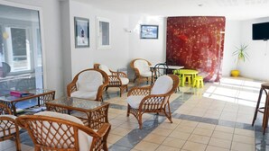 Une pièce avec des chaises en osier, une table en verre, une table jaune et un rideau rouge.