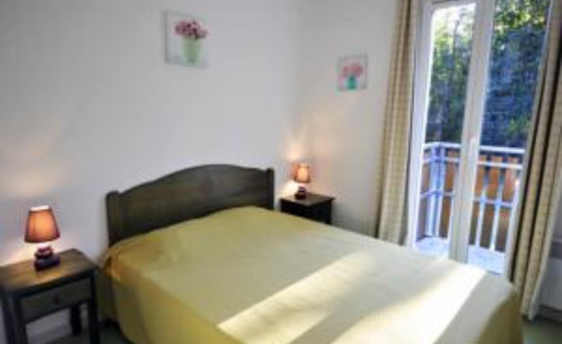 Une chambre à coucher avec un lit, deux tables de chevet avec des lampes et une vue sur l’extérieur par une fenêtre.