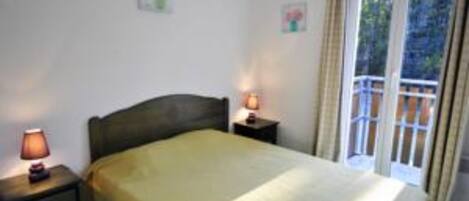 Une chambre à coucher avec un lit, deux tables de chevet avec des lampes et une vue sur l’extérieur par une fenêtre.