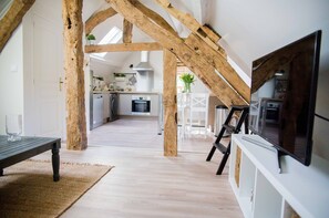 Un loft espaiós amb bigues de fusta a la vista, una cuina moderna i un gran televisor de pantalla plana penjat a la paret.