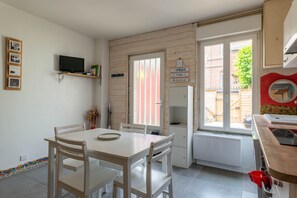 A small, well-lit kitchen with a dining table, chairs, a television, and a window with a view of the outside.