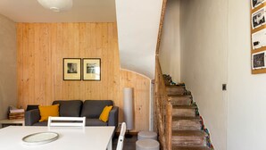 A modern living room with a wooden wall, a grey sofa, a white table, and a staircase with colorful steps.