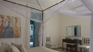 Een slaapkamer met een bed, een bureau, een stoel, een spiegel en een schilderij aan de muur.