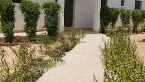 Een gebouw met een pannendak, een verharde opgang en een tuin met verschillende planten.