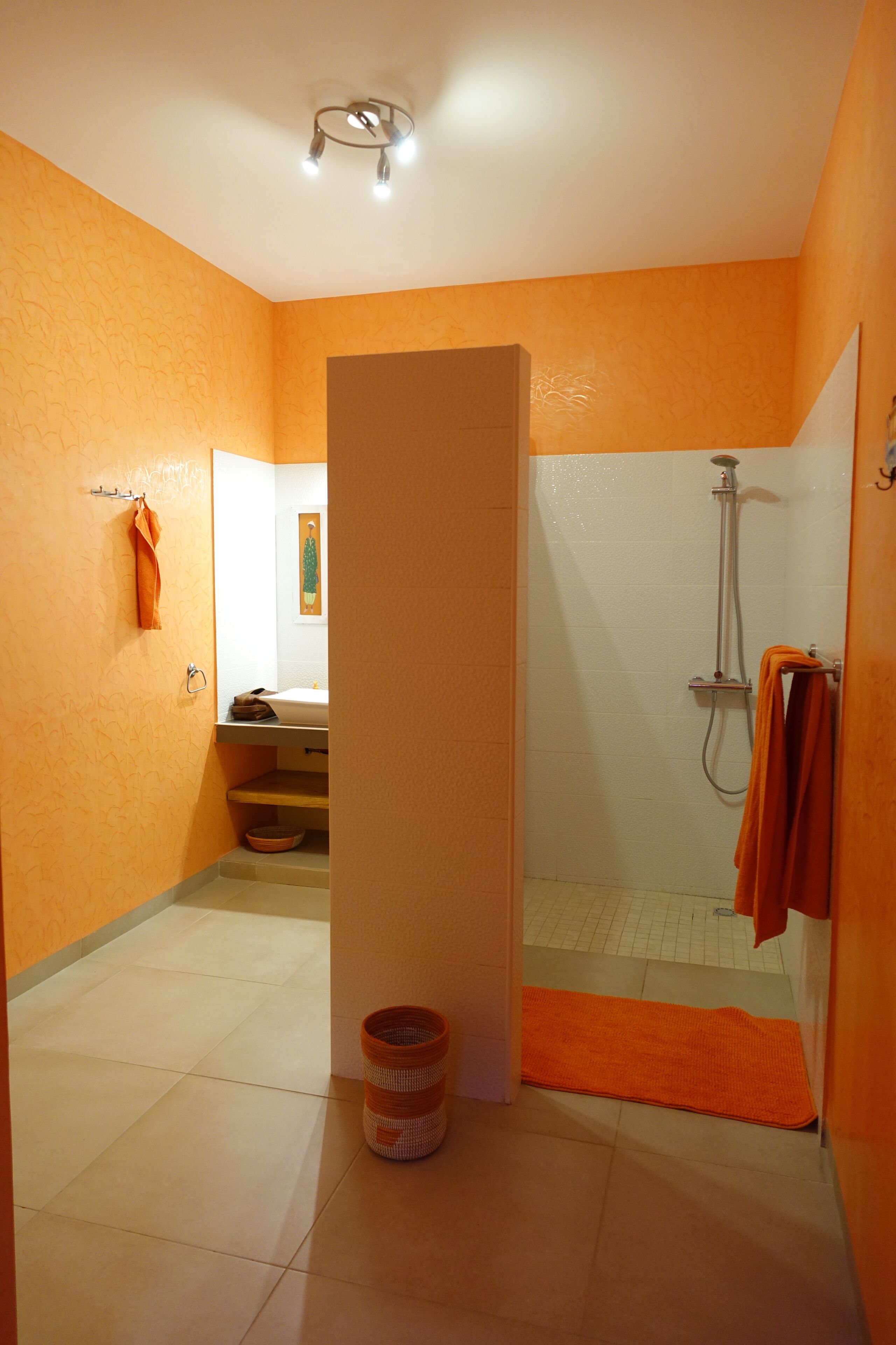 Ein Badezimmer mit orangefarbenen Wänden, einer Dusche, einem Waschbecken und einer Toilette.