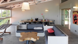 A modern living room with a hammock, a sofa, a coffee table, and a dining area with a table set for four. - Very beautiful luxury villa (Sainte-Luce)