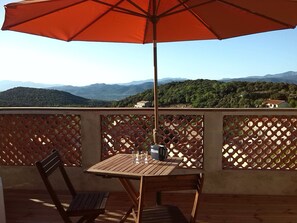 A wooden table with a metal bucket and a glass of water, under a red umbrella, on a balcony with a lattice railing. - Cottage for 2 persons (Bélesta)