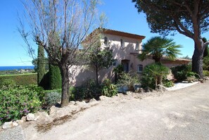 A two-story house with a tiled roof, surrounded by a garden with various plants and a palm tree.
