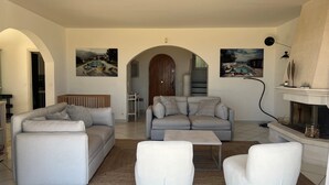 A living room with a grey sofa, a white armchair, and a coffee table. There is a fireplace and a painting on the wall. - Superb villa with panoramic sea view Sainte Maxime (Sainte-Maxime)