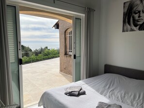 A bedroom with a bed, a view of the balcony, and a painting on the wall.