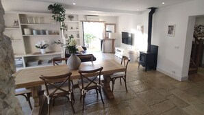 Un vaste espace de vie comprenant une table à manger en bois, des chaises, un canapé et un téléviseur. On y trouve également une cheminée et un mur en pierre.