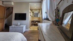Une chambre avec une commode en bois, un téléviseur fixé au mur, un escalier et une salle de bain équipée d’un miroir et d’un lavabo.