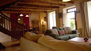 A cozy living room with a wooden staircase, a green sofa, and a dining area. - Charming 19th century house on the port of Dahouet (3 *) (Pléneuf-Val-André)