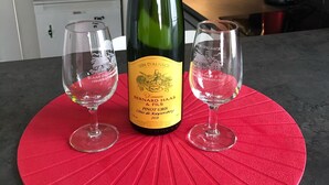 Punaisella alustalla on pullo Domaine Bernard Haas & Fils -viinitilan Pinot Gris -vuoden 2018 -viiniä, ja sen vieressä on kaksi lasia modernissa keittiössä.