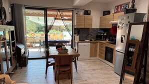 Een moderne keuken met een eethoek, houten keukenkastjes, een koelkast en een grote schuifpui die leidt naar een terras.