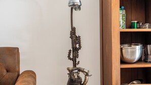 Een kamer met een bruine leren bank, een houten salontafel, een hoge metalen lamp en een houten kast met planken.
