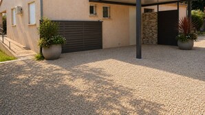 Uma casa moderna com varanda coberta, entrada de cascalho e plantas em vasos.